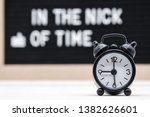 Small photo of black vintage alarm clock on the background of signs with the inscription in English in the nick of time