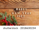 Happy New Year 2022. Quote made from wooden letters and numbers 2022 on wooden background dcorated fir tree branch with berries and cones. Creative concept for new year greeting card