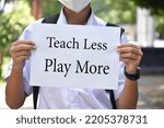 Small photo of Thai boy student holds protesting paper which has text 'Teach Less Play More', soft and selective focus, concept for calling all teachers to reduce teaching in class and increase playing outclass .