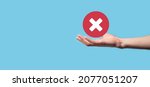 Small photo of Hand holds icon,cancellation symbol,cancel icon.Cross mark flat red icon.round X mark.cancel button.Wrong.cross mark rejection.Declined.On dark background.Banner.Copy space.Place for text