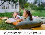 Small photo of Side view of girls lying on blanket, eating homemade popcorn and watching film on DIY screen from projector. Summer outdoor weekend activities with kids. Open air cinema. Outside movie night