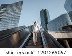 Stylish businesswoman in white suit going up on the escalator at the business centre outdoors with skyscrapers on the background in Paris