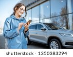Lifestyle portrait of a young stylish woman in blue coat using smart phone near the modern car outdoors