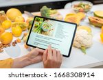 Woman looking on the digital recipe, using touchscreen tablet while cooking healthy meal on the kitchen at home, close-up view on the screen