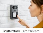 Woman rings the house intercom with a camera installed on the white brick wall