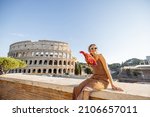 Portrait of a cheerful woman on background of Coliseum in Rome on a summer time. Concept of visiting famous landmarks and travel Italy. Girl wearing dress and colorful shawl