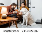 Men care their huge white dog at cozy home. Concept of homosexual relations and lifestyle at home. Idea of multinational gay families
