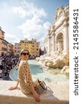 Small photo of Woman visiting famous di Trevi fountain in Rome. Traveling Italy on a summer day concept. Portrait of caucasian woman in dress and shawl in hair