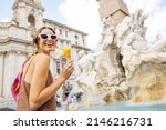 Small photo of Portrait of a cheerful woman eating ice cream in cone while visiting famous Navona square near fountain in Rome. Concept of happy summer vacations, traveling famous italian landmarks