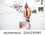Woman removes snow with a snow thrower machine near house at residential area. Winter yard care and easy technology concept