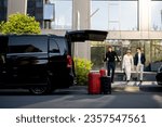Driver or concierge helps a business couple carry their suitcases to minivan taxi from hotel. Concept of business travel and transportation service