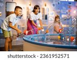 Mom with kids play with balls, learning physical phenomena in an interesting way, having fun in a science museum with interactive models