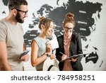 Small photo of Young couple of travelers choosing a summer strip standing with travel agent on the world map background