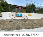 Small photo of Flowers in metal pots hung on the garden wall and decoration elements hung on the wall. Ornaments hung on the walls in the streets of Aegean village.