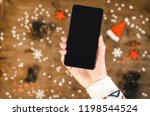 Female hands holding smart mobile phone with oled display on wooden background with Christmas gifts snowflakes and snow magic fairy tale light effect. Happy New Year and Xmas Flat lay