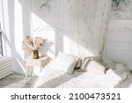 White cozy bedroom  where the sun shines from the window. White bedding, dried flowers in a vase on a bedside table for decoration.
