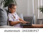 Small photo of Side view of happy and smart little girl using laptop at home. Five year old girl try to use smart devise