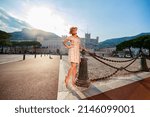 a bright beautiful girl in a light dress and hat walks along the streets of old town of Monaco in sunny weather, a residential area of principality and walking people in the background