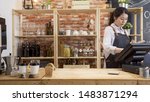 Small photo of small business people and service concept. happy woman waitress in apron at counter with cashbox working at coffee shop. young girl barista in modern cafe bar touching on touch pad checking order.
