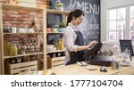 Small photo of smiling coffee shop assistant using pos point of sale terminal to put in order from note paper at restaurant register. waitress lady working in counter in cafe store. young girl staff using cashbox.
