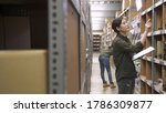 Small photo of two warehouse inventory manager women checking distribution in storehouse storage area. concentrated girl teamwork partners at work in stockroom. lady hold clipboard stock taking in depot of factory.