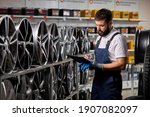 male salesman in auto shop making notes, checking the document and examining characteristics, looking at rack with auto rims