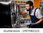 Small photo of bearded male auto mechanic in uniform is confidently checking car discs represented for sale in service, examining, keep tabs on merchandise