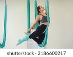 Young fit woman doing flying yoga stretch in turquoise hammock indoors. The concept of a healthy lifestyle. copy space, place for text