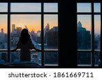 Young happy woman standing in the bedroom by the window with her back and beautiful sunrise or sunset and city scenery in the window. Copy space