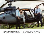 Beautiful woman getting down the helicopter with the help from her boyfriend. Couple disembarking their helicopter with pilot standing by.