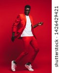 Small photo of Full length od handsome young african man dancing on red background. Man in stylish red outfit showing some dance moves.