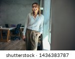 Smiling businesswoman standing in office. Online business owner in casuals standing by window in office looking away and smiling.