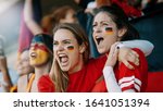 Female spectators cheering at sports event. Germany football team supporters actively cheering and chanting in crowd.