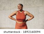 Plus size female model in sportswear smiling with her hands on hips. Positive woman relaxing after workout outdoors.