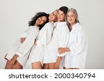 Models of different ages embracing their natural and aging bodies in a studio. Four confident and happy women smiling cheerfully while wearing mens shirts against a white background.