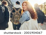 Female student glancing back while going for a class in college. Girl walking with friends going for class in high school.
