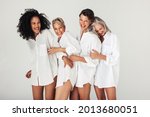 Studio shot of diverse women embracing their natural and aging bodies. Four confident and happy women smiling cheerfully while wearing white shirts against a white background.