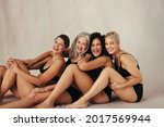Cropped shot of four women embracing their natural bodies. Women of all ages wearing black underwear and smiling cheerfully. Happy women sitting together against a studio background.