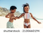Two cheerful little kids having fun and enjoying themselves at the beach. Two adorable ethnic kids smiling happily while playing around in swimwear.