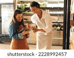 Small photo of Happy grocery store workers managing online grocery orders on a digital tablet. Empowered woman with Down syndrome running a successful supermarket with her female colleague.