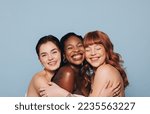 Small photo of Group of happy women with different skin tones smiling and embracing each other. Three diverse women feeling comfortable in their natural skin. Body positive young women standing together in a studio.