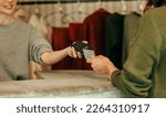 Small photo of Unrecognisable female customer paying with a credit card at the checkout counter. Young woman tapping a credit card on a contactless card reader. Woman purchasing clothes in a clothing store.