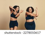 Small photo of Two young women, wearing sports clothing and full of vitality, dance and exercise together in a studio. Happy female athletes having fun and celebrating their fit lifestyle.