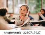 Small photo of Happy little girl learning to draw with a colour pencil in an elementary art class. Primary school kid talking to her teacher as she receives quality education in a positive learning environment.