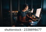 Small photo of A focused businessman works late in a well-lit office, typing on his laptop. Surrounded by a busy workplace, he diligently focuses on a marketing plan, driven by ambition and dedication.