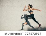 Young woman with fit body jumping and running against grey background. Female model in sportswear exercising outdoors.