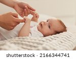 Adorable little baby holding fingers of mother when lying on soft blanket bed