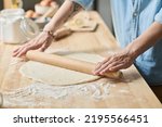Close-up of young woman rolling dough with rolling pin for homemade bakery at table