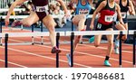 Small photo of Front view of four high school girls running in a hurdle track and field race.