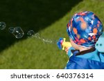 A boy in blue jacket and hat blows bubbles from toy bubble gun.Selective focus on the toy